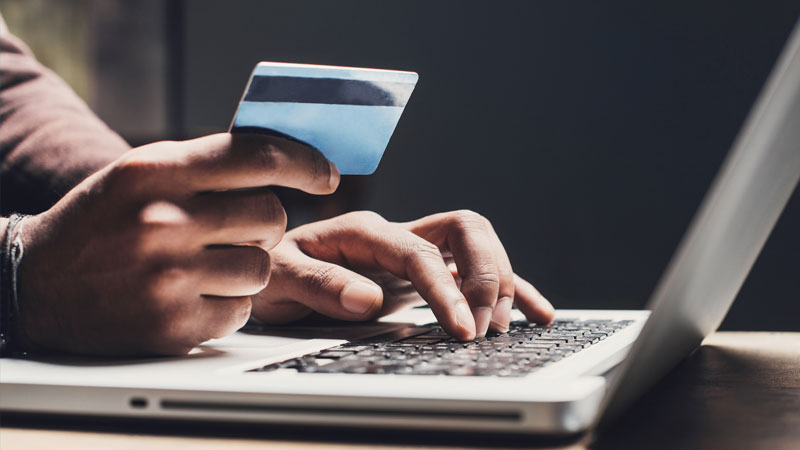 Mãos seguram um cartão de crédito e escrevem num portátil